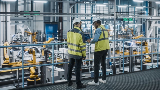 Two workers in safety gear oversee an automated factory floor